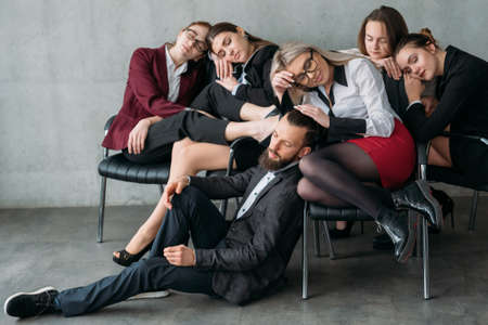 Money making workaholics. Accounting period. Overworked females sleeping on chairs with man teamlead on floor.の写真素材