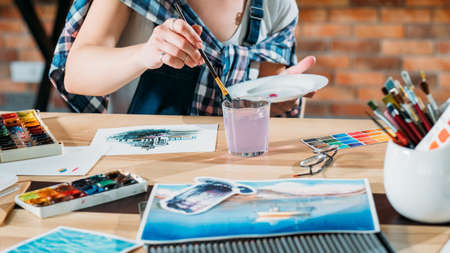 Studio workplace. Artist at work. Painter doing watercolor painting. Sketchbook and palette supplies around.の写真素材