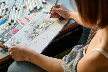Artist sketching. Workplace inspiration. Woman painter drawing in sketchbook with palette and supplies around.の写真素材