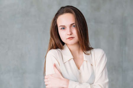 Woman facial expression. Young beautiful female looking wearily feeling cold. Copy space on grey background.の写真素材