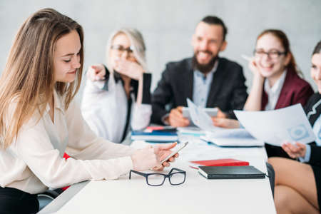 Business meeting. Paperwork. Team members laughing at daydreaming colleague checking smartphone.の写真素材