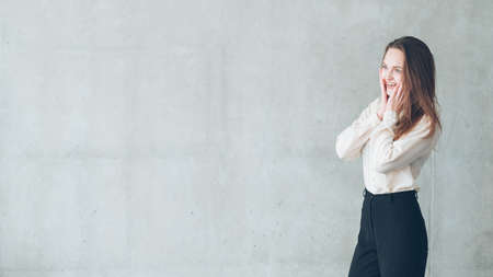 Excited young woman. Beautiful female looking at virtual advertisement with hands at face. Copy space on grey background.の写真素材