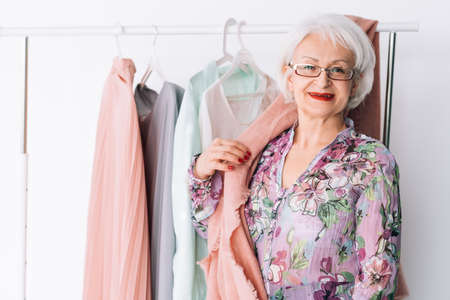 Senior lady wardrobe. Shopping and clothing options. Smiling elderly woman choosing trendy outfit.の写真素材