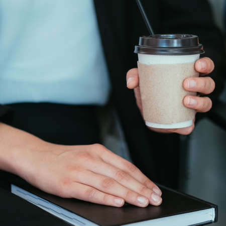 Coffee break at work. Woman with cup and notepad in hands. Cropped shot.の写真素材