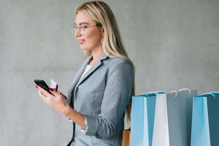 Online banking. Credit card payment. Young woman with smartphone and shopping bags variety.