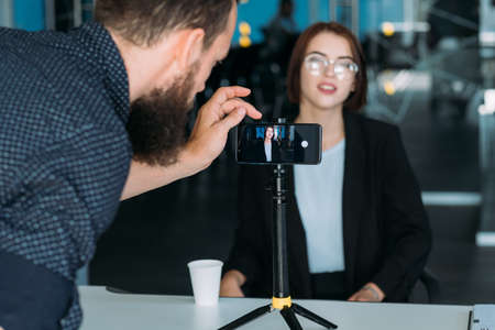 Business master class. Woman coach. Man assistant with smartphone. Mobile video shooting of workshop.の写真素材