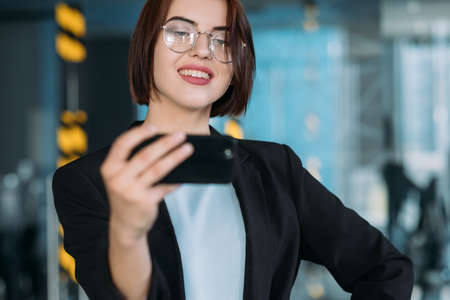 Confident business lady. Office workspace. Beautiful young woman hand on hip taking selfie.の写真素材