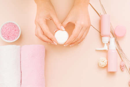 Hands beauty care. Assorted cosmetic products on coral pink background. DIY treatment. Woman with cream jar.の写真素材