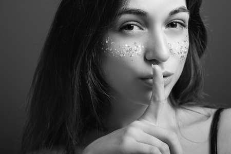 Shush gesture. Secret. Pretty female with finger at lips. Sly expression. Black and white portrait.の写真素材