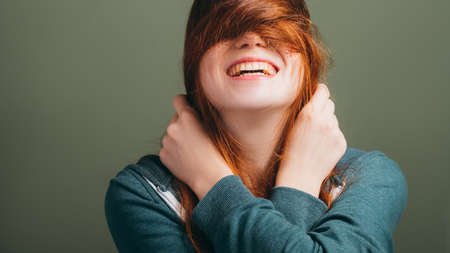 Redhead female expressing joy emotion. Young woman with toothy smile messing hair. Copy space on green background.の写真素材