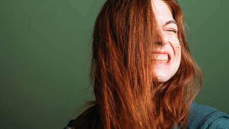 Woman emotion. Facial grimace. Young redhead female with bared teeth. Copy space on green background.の写真素材