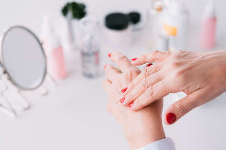 Beauty care senior blogger. Age hand skin products. Elderly lady applying expensive cosmetics.の写真素材