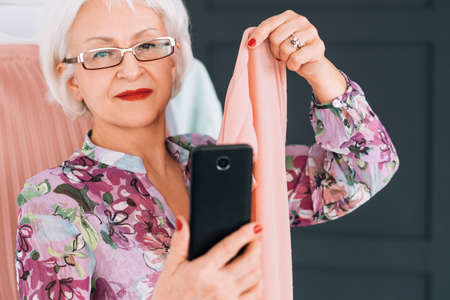 Senior lady fashion blogger. Trendsetter lifestyle. Elderly woman taking selfie analyzing color type.の写真素材