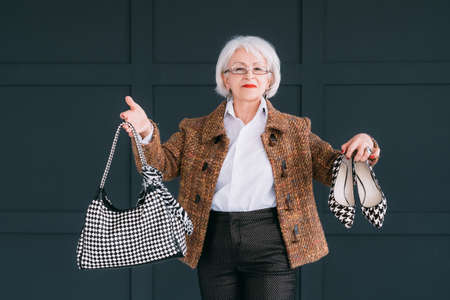 Senior fashion stylist. Personal consultant on trendy wardrobe. Confident aged lady posing with bag and shoes.の写真素材