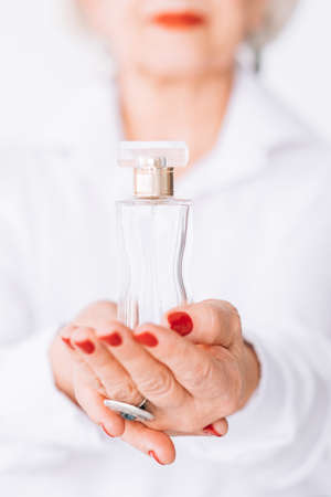 Senior lady lifestyle. Fragrance choice. Bottle of expensive perfume in female hands.の写真素材
