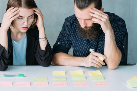 Business strategy failure. Troubleshooting. Concerned man and woman analyzing ideas. Post it notes on desk.の写真素材