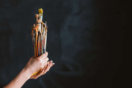 Painter tools set. Work and lifestyle. Assorted brushes bunch in woman hands. Copy space on black background.の写真素材