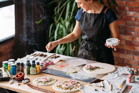 Clay art. Ceramic craft. Creative artist studio atmosphere. Woman with modeling tools at workplace. Incense smoke.の写真素材