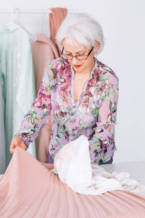 Confident senior lady at work. Fashion boutique business success. Elderly lady analazing color matching at showroom workplace.の写真素材