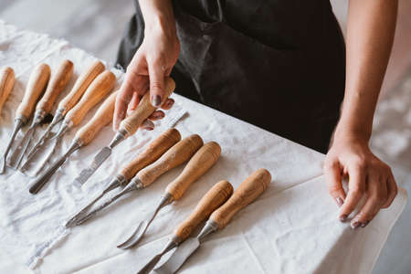 Carving tools assortment. Craft set composition arranged on table. Woman hand choosing chisel.の写真素材