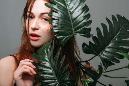 Beauty treatment. Organic cosmetics care. Young pretty woman with monstera. Natural makeup. Glitter freckles.の写真素材