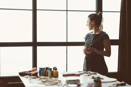 Rest and contemplation time. Artist inspiration. Craft woman with mug looking thoughtfully at window. Copy space.の写真素材