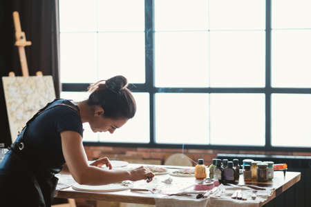 Artist at work. Studio workplace. Ceramic artwork in process. Handicraft. Woman with modeling tools in hands.の写真素材