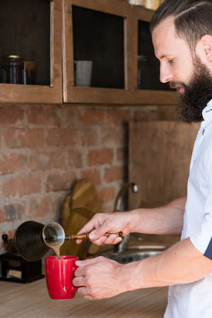Morning. Coffee making time. Young hipster lifestyle. Man with jezve pouring latte into red cup.