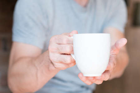 New day. Morning wake up drink. Coffee time. Man offering white cup of energy beverage.の写真素材