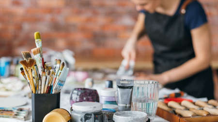 Artist workplace. Brushes, bottles and modeling tools. Art craft. Female in apron working in studio....