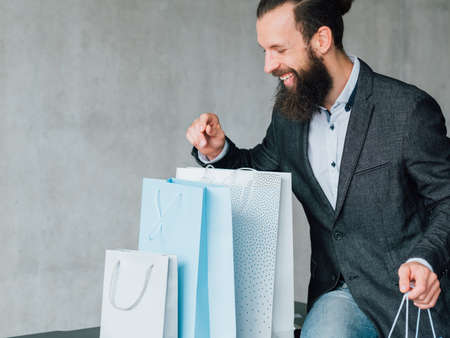 Shopping joy. Black Friday sale. Excited young bearded man with bags variety. Copy space on grey background.の写真素材