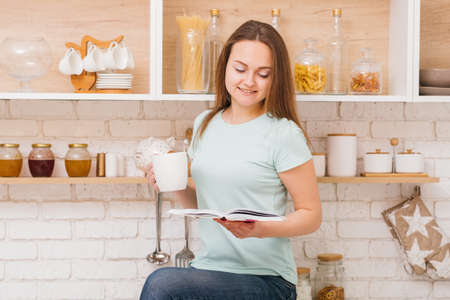 Relaxed home leisure. Woman drinking tea and reading a book in cozy kitchenの写真素材