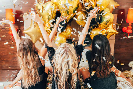 Women night out. Party leisure time. Females on bed catching glitter confetti and balloons. Youth joy and freedom.の写真素材