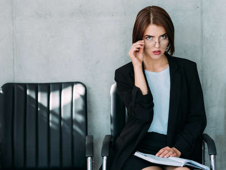 Successful career. Young pretty business lady sitting with notebook, removing eye glasses. HR manager waiting for job applicant.の写真素材