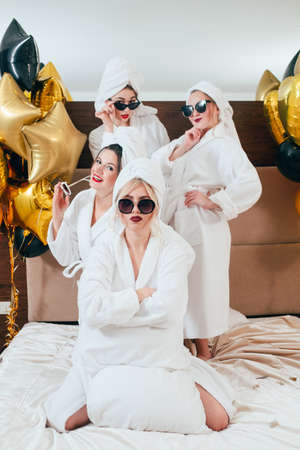 Not sure. Young woman with folded arms. Incredulity and doubt. Friends behind. Girls bathrobe party. Balloons decor.の写真素材