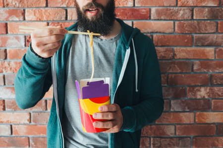 Millennials nutrition. Hipster guy eating chinese noodles with chopsticks. Takeaway lunch meal. Food...