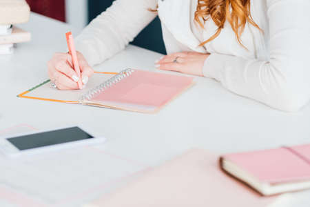 Woman workplace. Comfy home office. Female making notes in diary while planning day. Notebooks, smartphone at hand.の写真素材