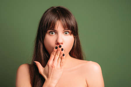 Ashamed beautiful woman. Surprised facial expression. Closeup portrait of emotional brunette girl covering mouth with hand.の写真素材