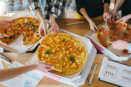 Pizza time. Youth eating habit. Business team lunch. Group of colleagues friends taking slices. Unhealthy delicious meal.の写真素材
