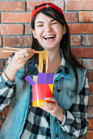 Youth eating habit. Takeout food. Excited female millennial with Chinese noodles. Yummy spicy meal, unhealthy nutrition.の写真素材