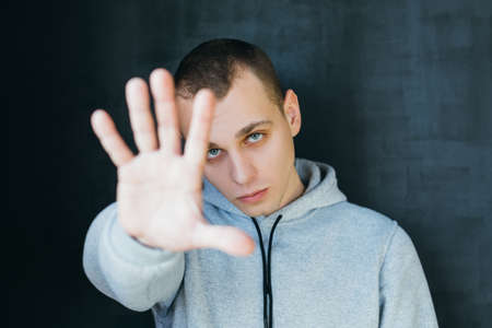 Enough. Serious handsome guy making stop gesture. Moody young man in grey hoody. Fixed gaze. Personal privacy.の写真素材
