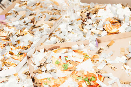 After party mess. Closeup of pizza, doughnut leftovers covered with shiny confetti. Half empty...