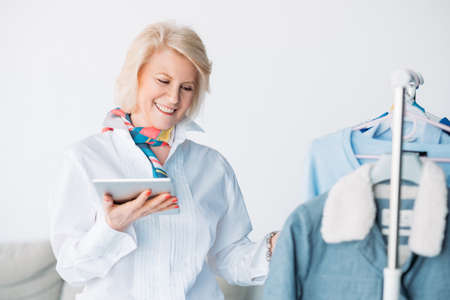 Successful seniority. Showroom clothes business. Smiling lady with tablet at work. Money making...