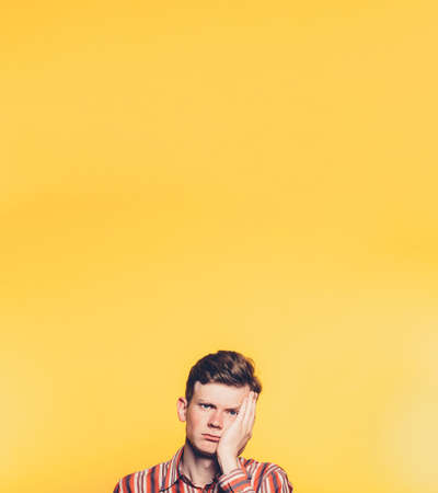 Bored man portrait. Disappointed facial expression. Man with hand on cheek over yellow background....