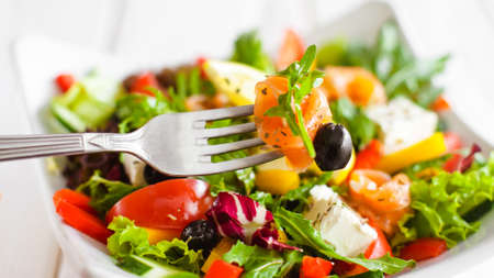 Healthy nutrition lifestyle. Closeup of rolled salmon slice on fork. Blurred vegetable salad background.の写真素材