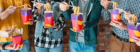 Millennials lunch. Cropped shot of young people eating unhealthy noodles at work. Junk food addiction. Busy generation.の写真素材