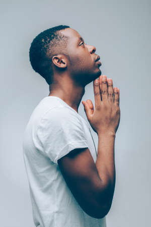 Religion and faith. Side view of afroamerican guy praying God, hoping for better. Man asking for good luck, success, forgiveness.の写真素材