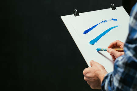 Contemporary art. Closeup of sketch board with blue acrylic paint lines. Talented artist creating...