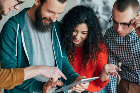 Great job. Project success. Group of happy millennials looking at tablet. Diverse business team....