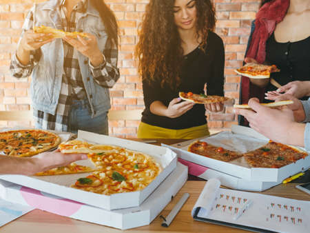 Young creative business team. Lunch break. Men and women eating pizza. Unhealthy junk food lifestyle of busy millennials.の写真素材